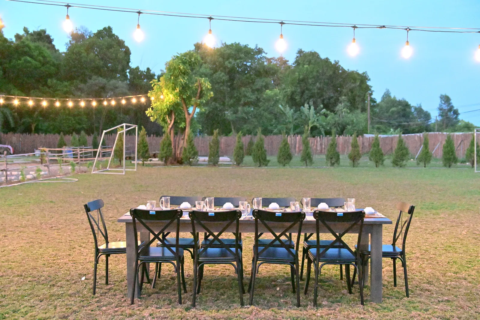An outdoor dining table set for a party beneath warm string lights at dusk