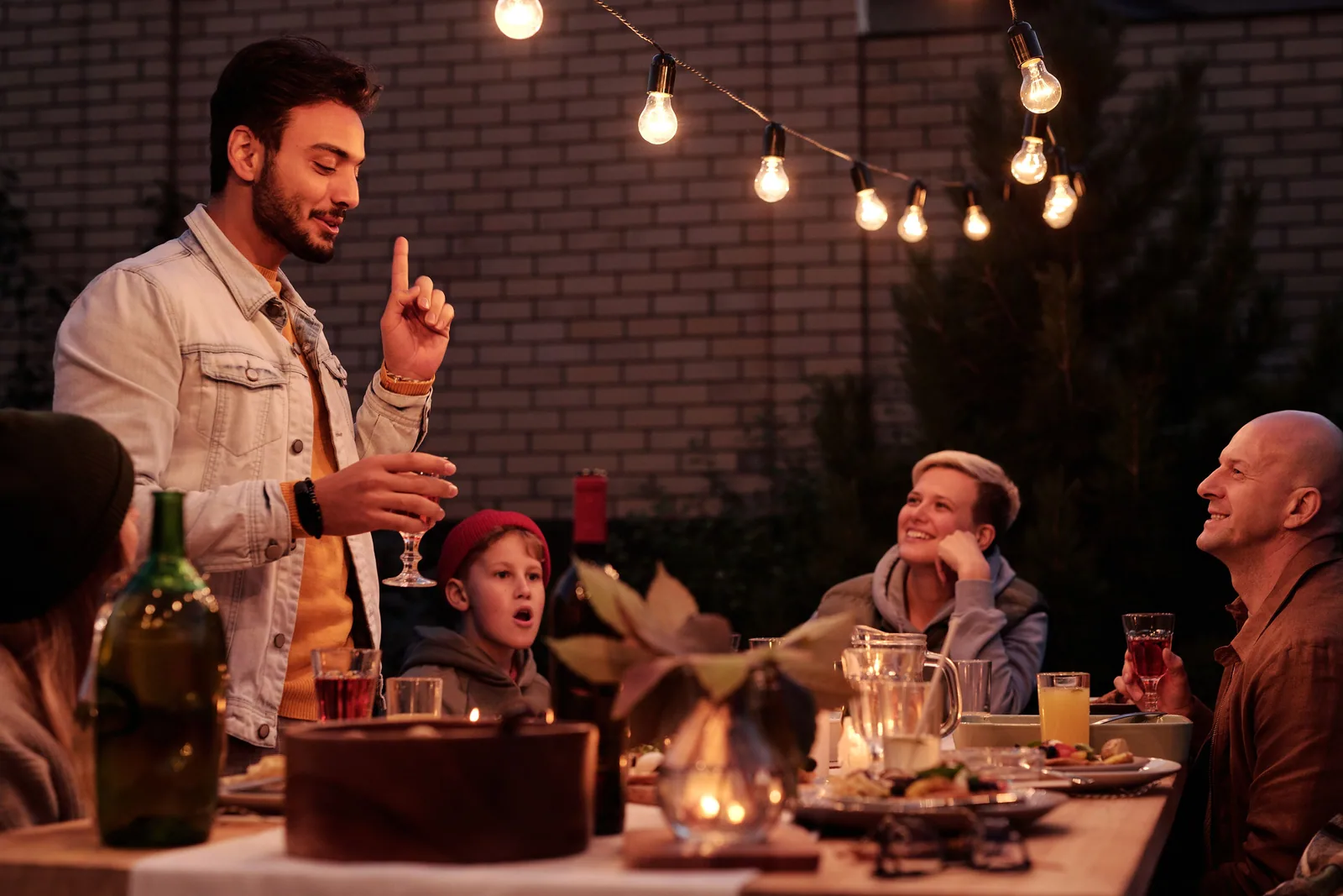 A group of friends laughing together at a candlelit outdoor dinner table