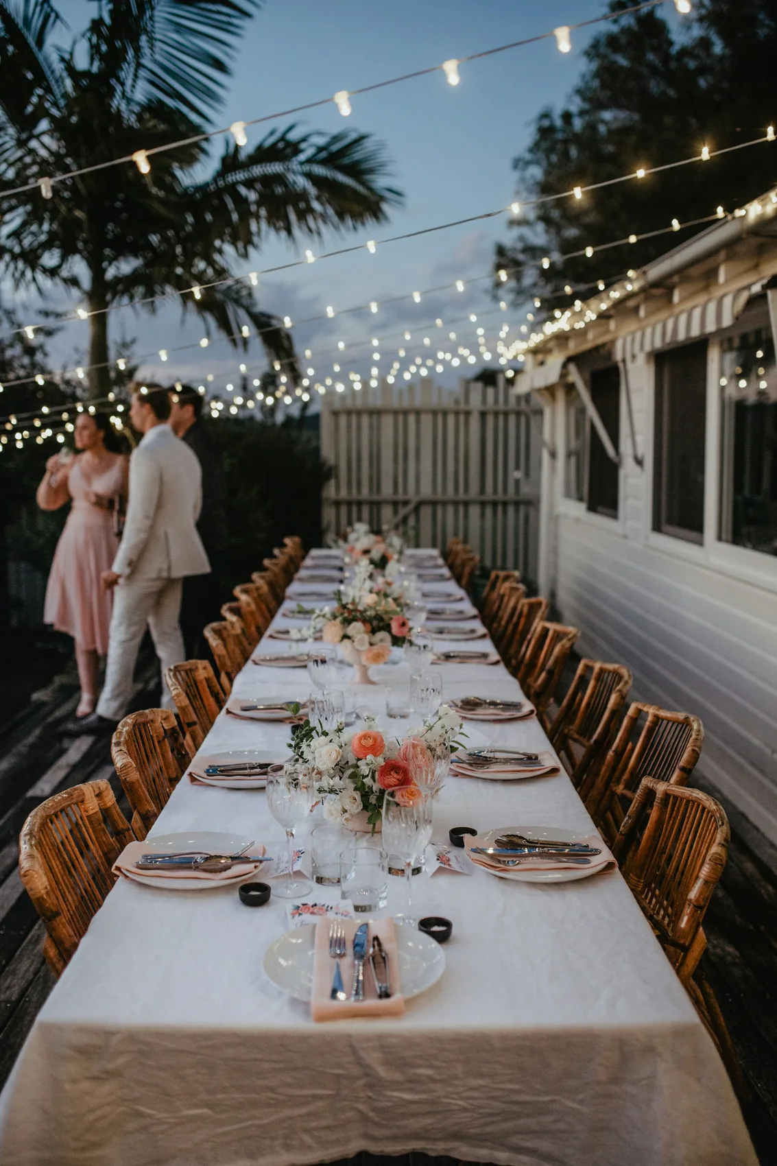A long table laid with linen, flowers and glassware beneath strings of lights